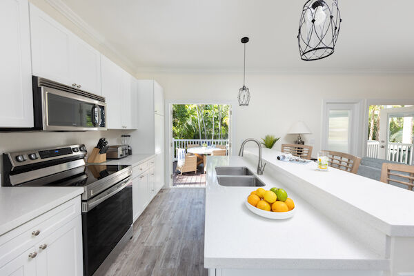 A modern kitchen with white cabinets, stainless steel appliances, and fruit on the counter, leading to a patio with outdoor seating.